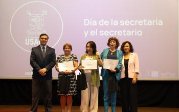 Rector (S), secretarias premiadas y Vicerrectora en escenario del Aula Magna