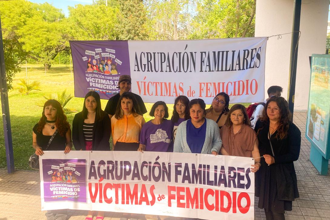 Grupo de personas ubicadas afuera de casa central, principalmente mujeres incluida la Vicerrectora de Calidad de Vida, Género, Equidad y Diversidad, doctora Karina Arias quien está al centro., que portan un lienzo que dice Agrupación Familiares de Víctimas de Femicidio