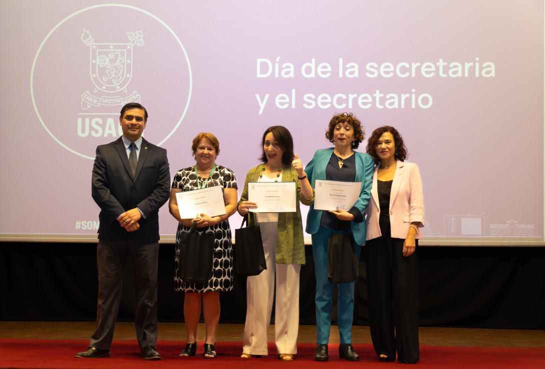 Rector (S), secretarias premiadas y Vicerrectora en escenario del Aula Magna